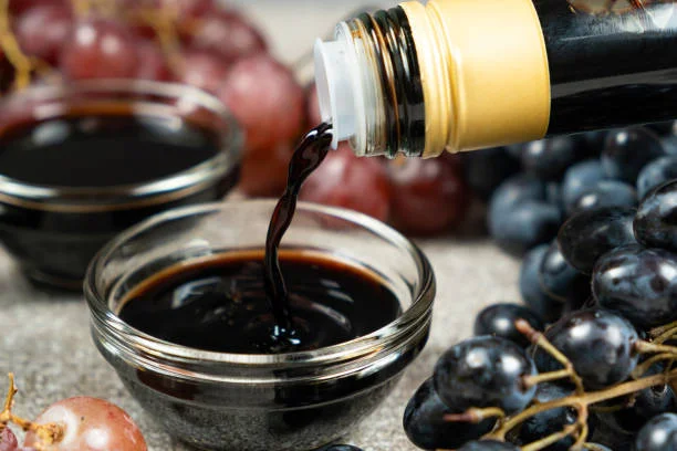 bottle of balsamic vinegar beside olive oil tomatoes fresh herbs on rustic wooden table