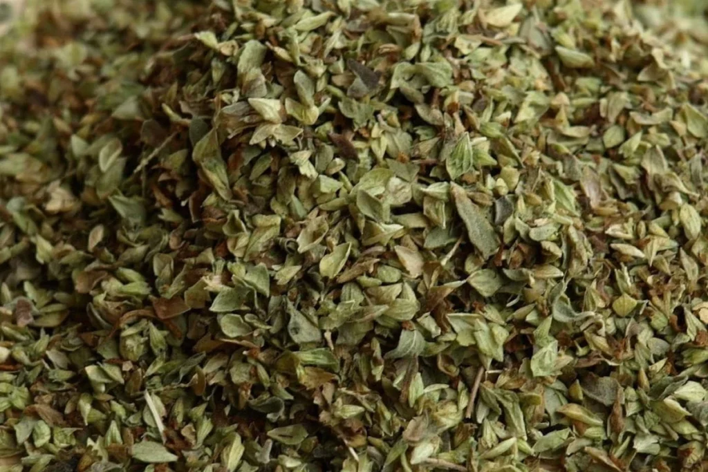 dried oregano in small cream ceramic bowl with fresh oregano sprigs on rustic wooden table warm