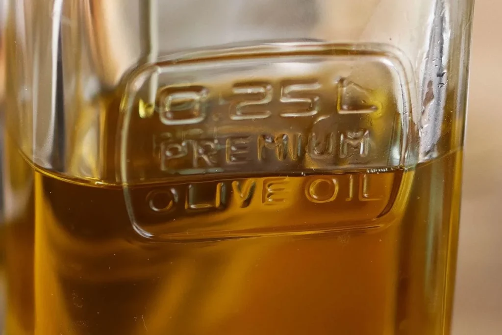 bottle of extra virgin olive oil beside fresh herbs garlic and rustic wooden kitchen 