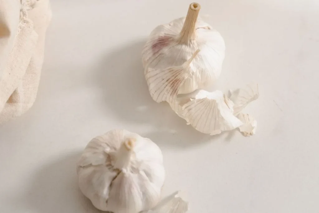 fresh garlic bulbs and cloves on rustic wooden kitchen table beside olive oil warm golden tones overhead