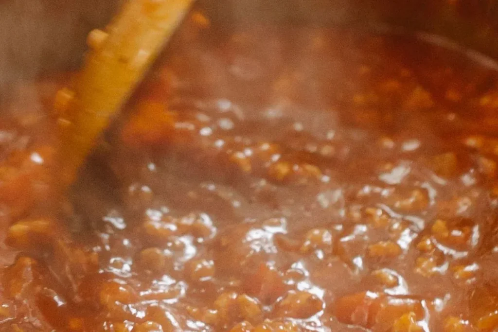 breadcrumbs being stirred into thick pasta sauce wooden spoon saucepan