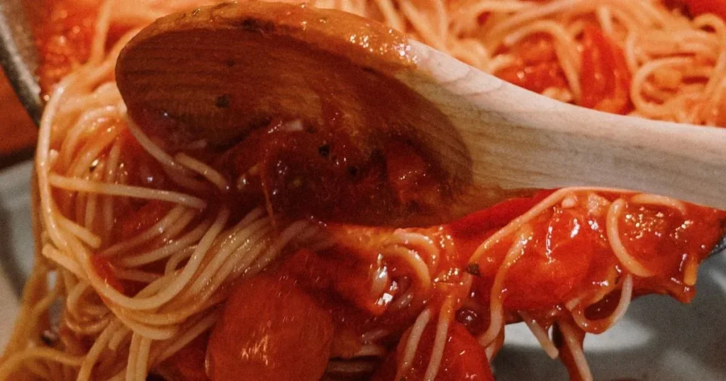 thick rich Italian pasta sauce coating spaghetti in white ceramic bowl rustic wooden table overhead