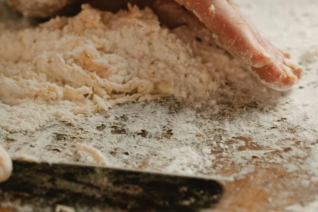 Why Is My Pizza Dough So Sticky? (9 Easy Fixes That Actually Work) 6 Metal dough scraper lifting sticky pizza dough from a wooden work surface